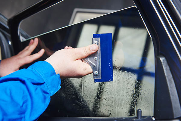 car tinting. Automobile mechanic technician applying foil on  window in repair garage workshop