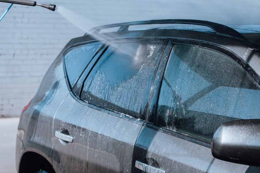 Wash or cleaning concept. Car parts being washed with water hose outdoors with sun flare