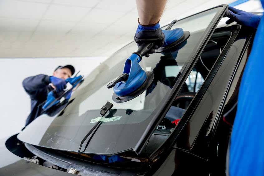 Automobile special workers replacing windscreen or windshield of a car in auto service station garage. Background