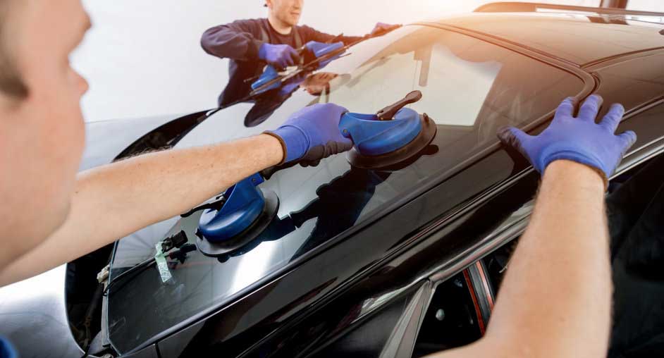 Automobile special workers replacing windscreen or windshield of a car in auto service station garage. Background