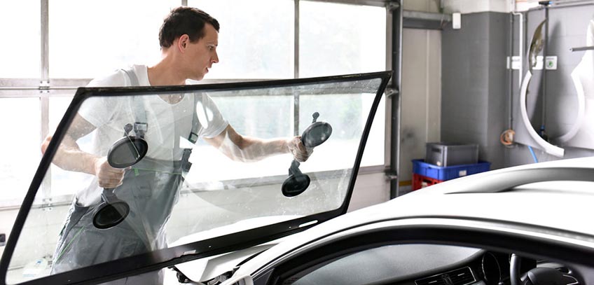 mechanic in a garage replaces defective windshield of a car