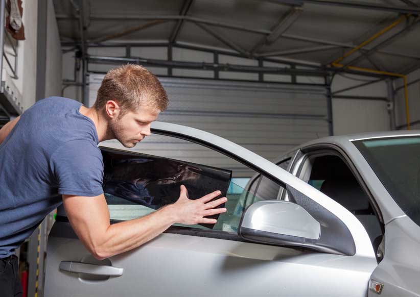 Applying tinting foil onto a car window in a workshop