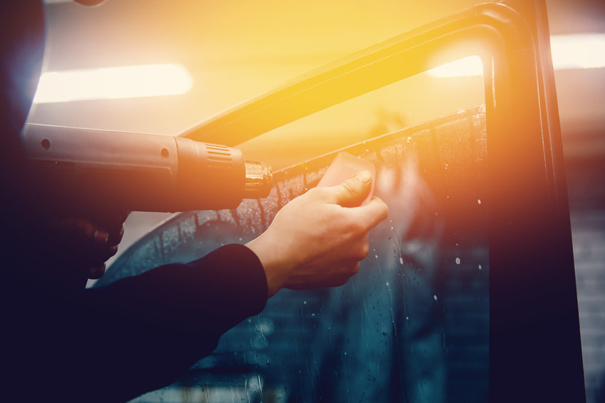 Master installs a tint film for the car glass with a hairdryer and spatula with glare of light. Concept tinting car. Toning and highlighting.