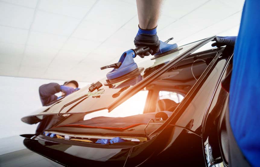 Automobile special workers replacing windscreen or windshield of a car in auto service station garage. Background