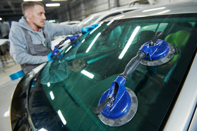 Glazier repairman mechanic worker replaces windshield or windscreen on a car in automobile workshop garage