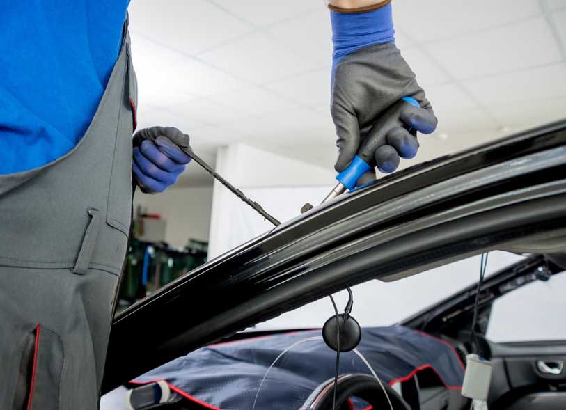 Automobile special workers remove old windscreen or windshield of a car in auto service station garage. Background