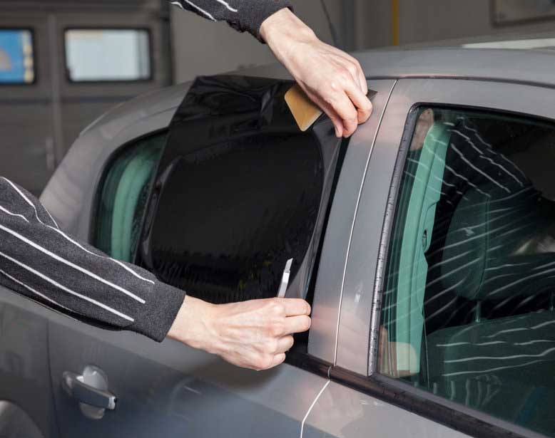 Applying tinting foil on a car window in a garage