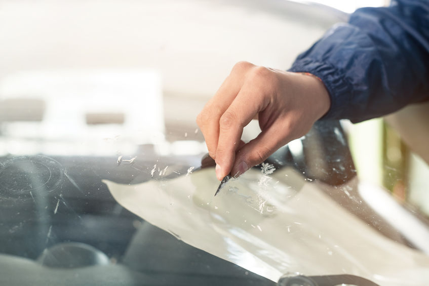 Close up Automobile glazier worker fixing and repair windscreen or windshield of a car in auto service station garage.