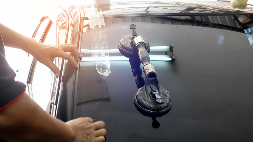 Automobile special workers replacing windscreen or windshield of a car in an auto service station garage.