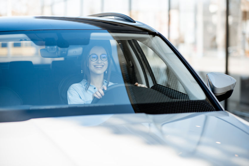 Young and happy woman driving a luxury car in the city, front view through the windshield